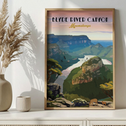 A framed vintage-style travel poster of Blyde River Canyon in Mpumalanga, South Africa, leaning against a white wall on a white shelf next to a vase with dried grass and a small candle.