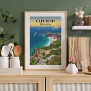 A framed vintage-style travel poster of Cape Point, Western Cape, displayed on a light wood countertop in a kitchen setting with a green hexagonal tile wall background.