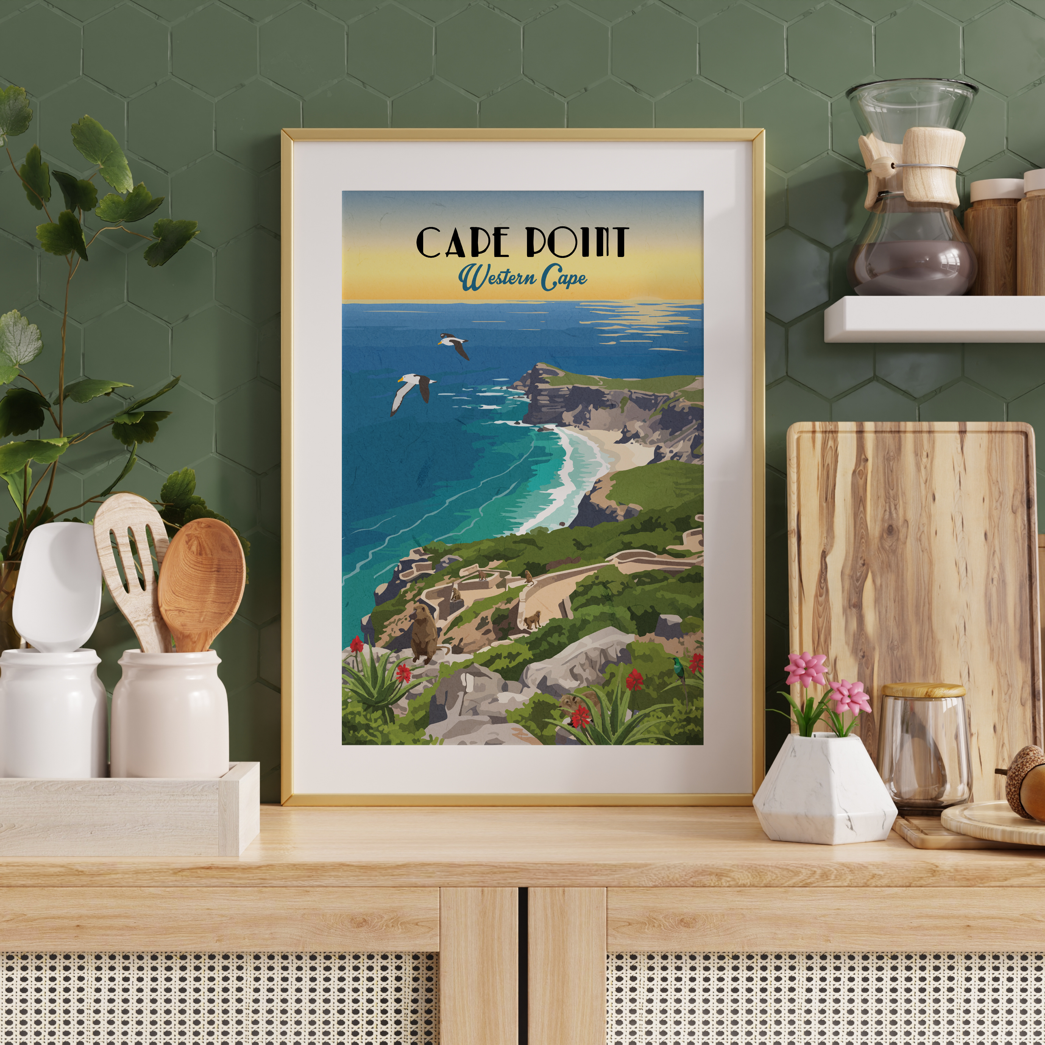 A framed vintage-style travel poster of Cape Point, Western Cape, displayed on a light wood countertop in a kitchen setting with a green hexagonal tile wall background.
