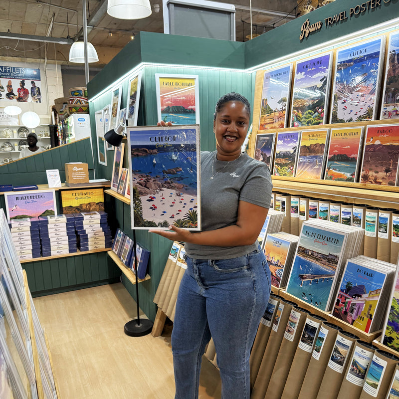Woman holding a Clifton Roam travel poster in a store with various posters on display.