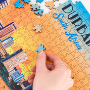 Hand placing a puzzle piece on a partially completed puzzle with colorful graphics and text.