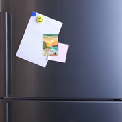 Black refrigerator with a paper attached to it, featuring a smiley face magnet and a scenic magnet of Knysna.