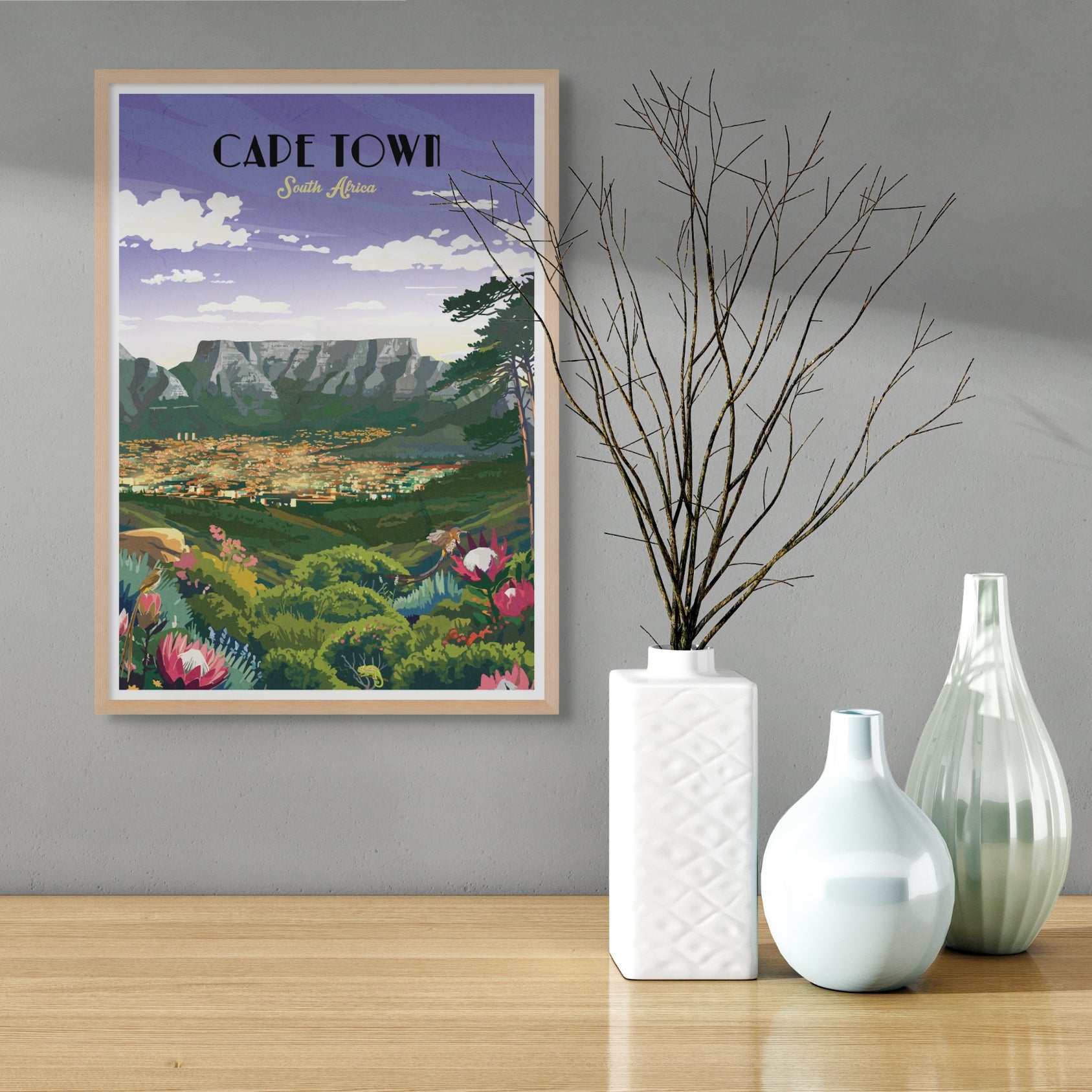 Framed poster of Cape Town on a wall with decorative vases on a table below.