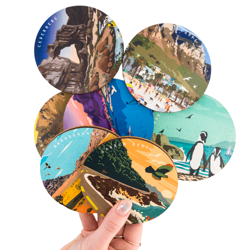 Set of round wooden South African Coaster with various scenic and nature-themed designs held by a hand.