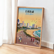 A framed travel poster of Durban, South Africa, leaning against a white wall on a light wood floor next to a white curtain. The poster features a retro-style illustration of the coastal city and beach at sunset, enclosed in a light natural wood frame.