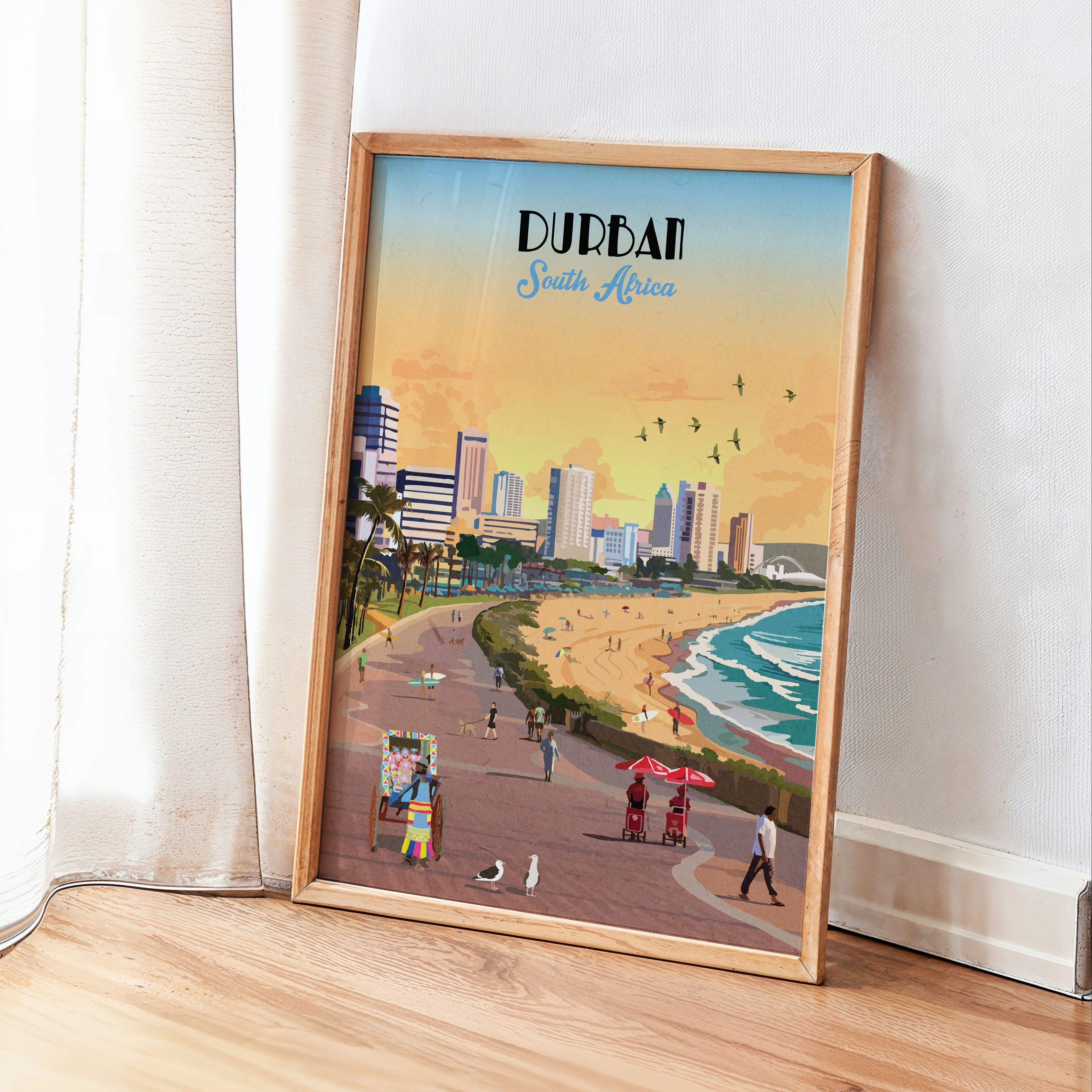 A framed travel poster of Durban, South Africa, leaning against a white wall on a light wood floor next to a white curtain. The poster features a retro-style illustration of the coastal city and beach at sunset, enclosed in a light natural wood frame.