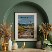 A framed art print of Drakensberg, South Africa, styled on a wooden shelf against a textured green wall with dried plants and decorative vases.