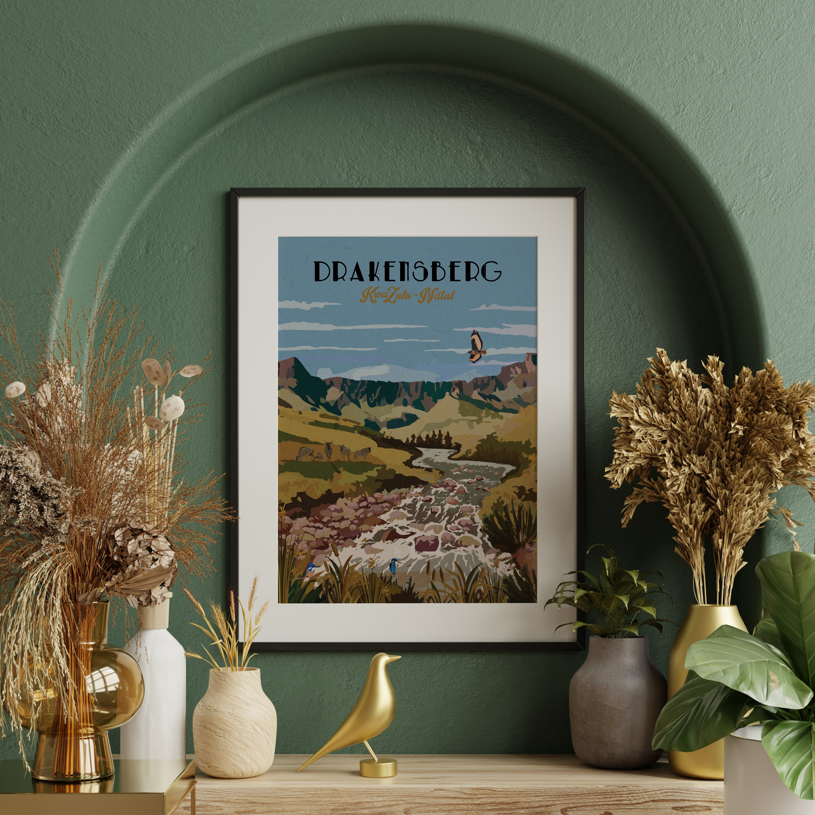 A framed art print of Drakensberg, South Africa, styled on a wooden shelf against a textured green wall with dried plants and decorative vases.