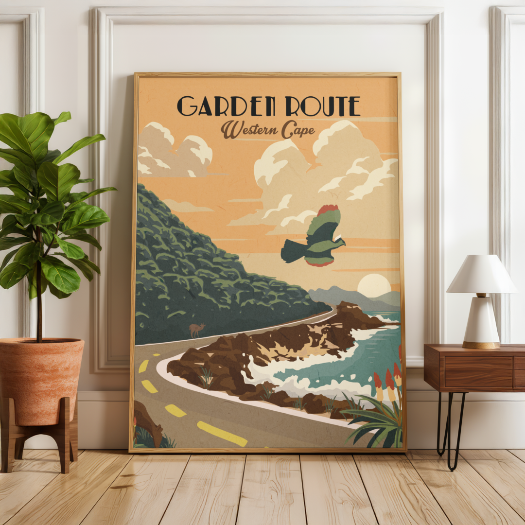 A framed vintage-style travel poster reading 'GARDEN ROUTE Western Cape' leans against a white wall in a styled room with a potted plant on the left and a small table with a lamp on the right.