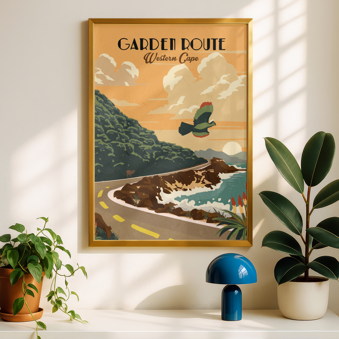 A framed vintage-style travel poster reading 'GARDEN ROUTE Western Cape' hangs on a white wall above a shelf with plants and a blue lamp. The poster depicts a coastal road scene with green hills, blue water, and a bird in flight.